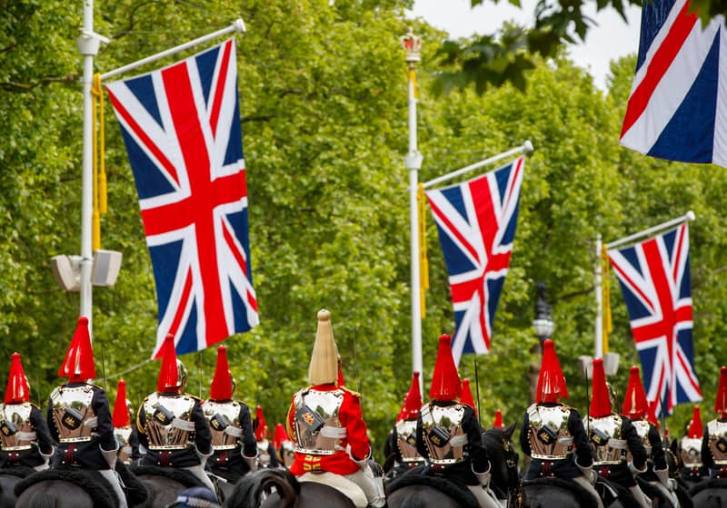 The Household Cavalry in gleaming uniforms parades beneath Union Jack flags in a grand display of British pageantry.