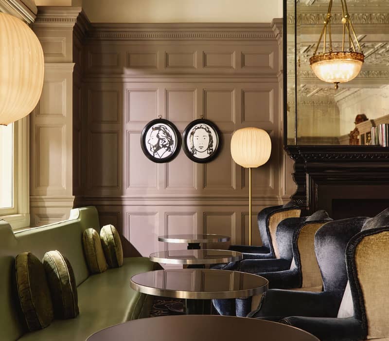 Sophisticated lounge with green and velvet seating, contemporary portraits, and ornate ceiling details reflecting timeless elegance