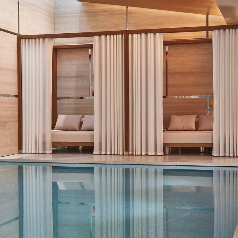 Elegant poolside cabanas with sheer curtains and plush seating, surrounded by warm wood tones, offering a serene, private oasis.
