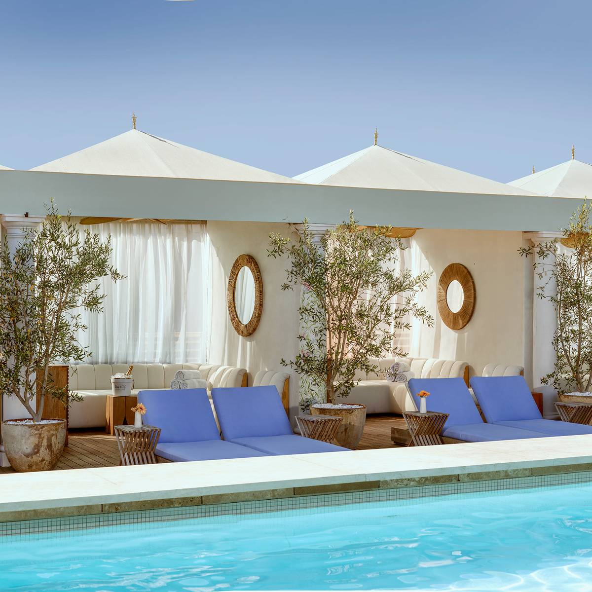 A serene rooftop pool oasis with plush cabanas, flowing curtains, and vibrant blue loungers, embodying effortless luxury under a clear sky.