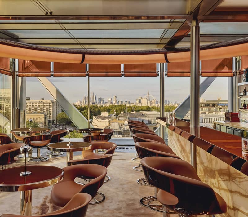 Stylish rooftop bar with sleek seating, a polished marble counter, and panoramic city views framed by floor-to-ceiling windows.